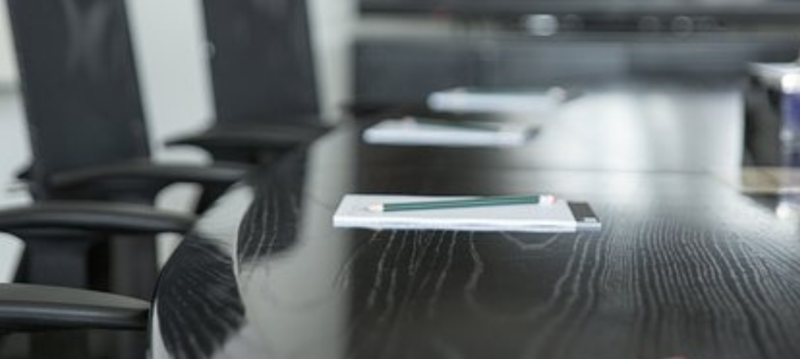 Close up photo of a board room table with a notepad and pen at each chair.